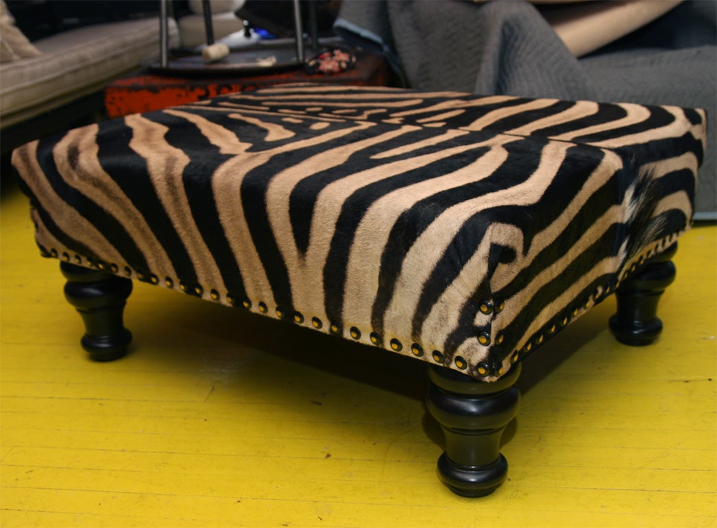 Supple Zebra skin ottoman in three tones: creme, grey, and dark brown/black. Legs of ottomon are tapered shape wood. Pelts are aquired directly from a Tanzanian reserve according to culling schedule. Soft, luxurious, tricolor skin.