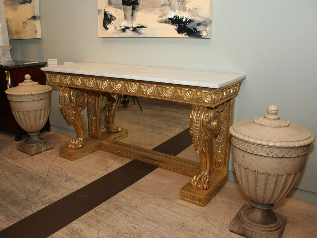The rectangular marble top over an ornately carved cornice shaped apron supported by two robustly carved hairy paw feet embellished with acanthus leaves and beading, the mirrored backplate flanked by carved panels all raised on a giltwood plinth