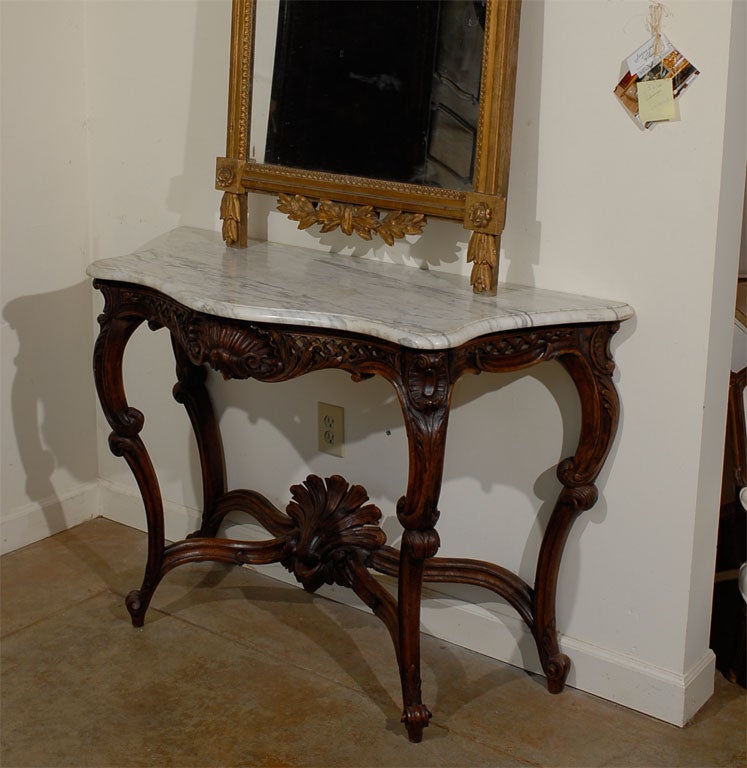 A French Régence style walnut console table from the 19th century, with grey marble top and carved apron. Born in France during the politically dynamic 19th century, this console table presents the stylistic characteristics of the Régence style that