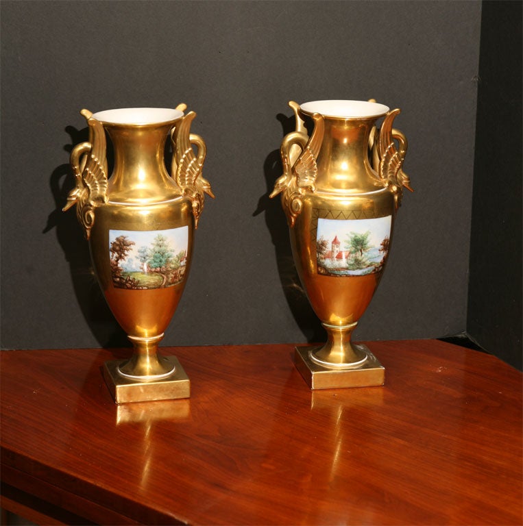 A very decorative pair of gilded porcelain vases manufactured by Dresden in the early part of this century to simulate fine Old Paris vases. The scenic painting different on all four sides is hand done and the gilding is in very good condition.