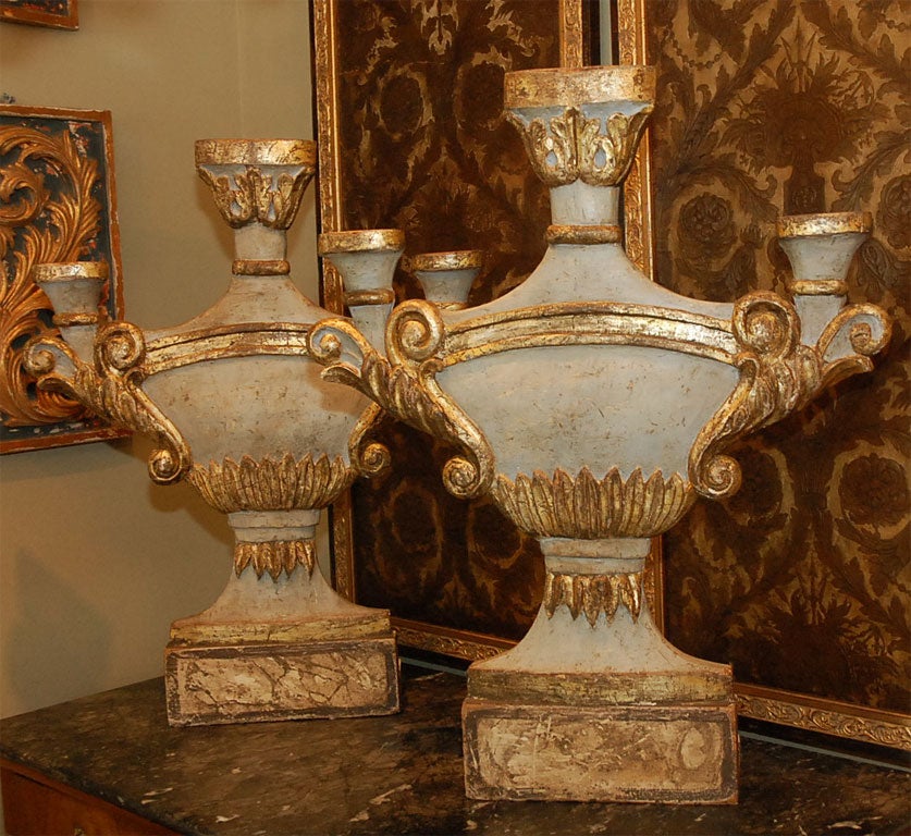 This unique pair of carved parcel gilt and painted urns are decorative but can be functional.  The generous size could cover unused fireplaces in the summer months.  Presented in the New Classical style, a pale robin egg blue remains.  The