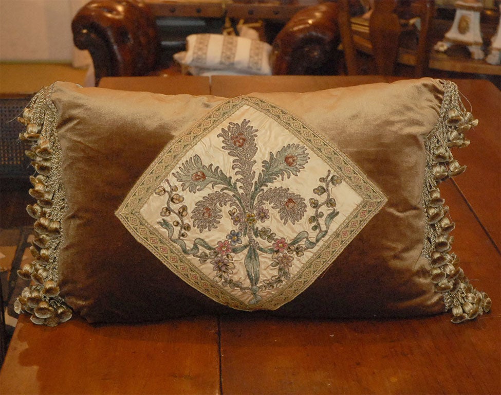 Custom pair of 19th century French metallic & chenille embroidered silk pillows depicting a bouquet of feathers intertwined with ribbon, garlands, and vines centered on a rootbeer colored silk velvet background with an ample amount of tassels seen