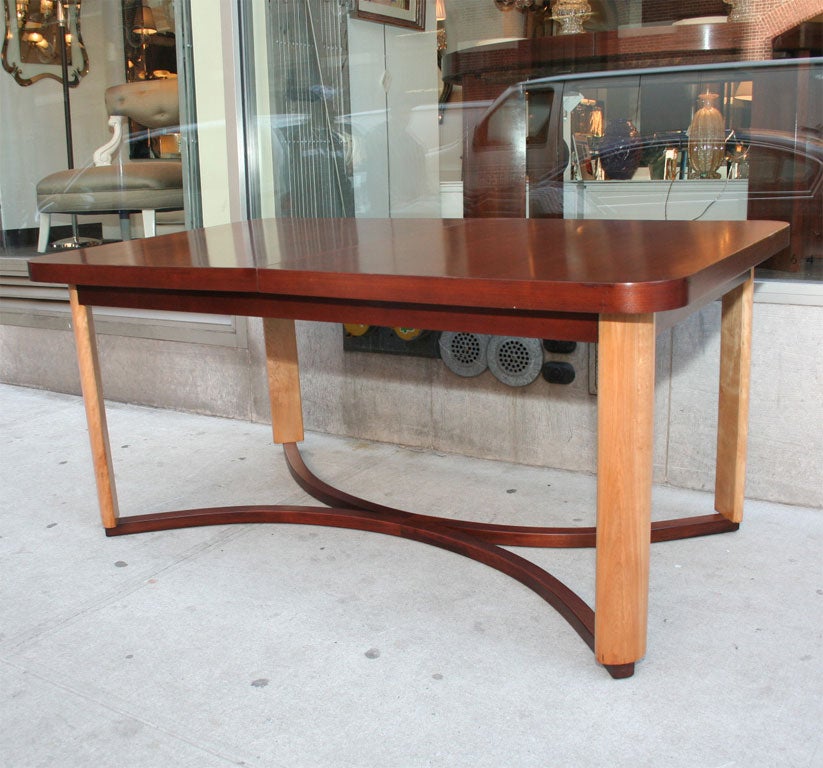 Designed by the illustrious American master Gilbert Rohde, circa 1935, this two-toned dining table features a rich burnished walnut top and elegantly curved hand rubbed birch legs which are connected at the base by two demilune shaped walnut