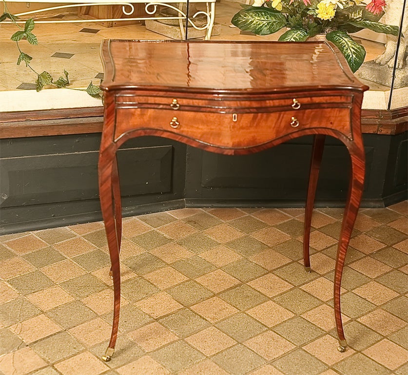 This very fine mahogany writing table made in England in the French taste would have been for only the most current and fashionable people of the time. The table has a serpentine top that opens to reveal a fitted interior all banded in ebony trim.