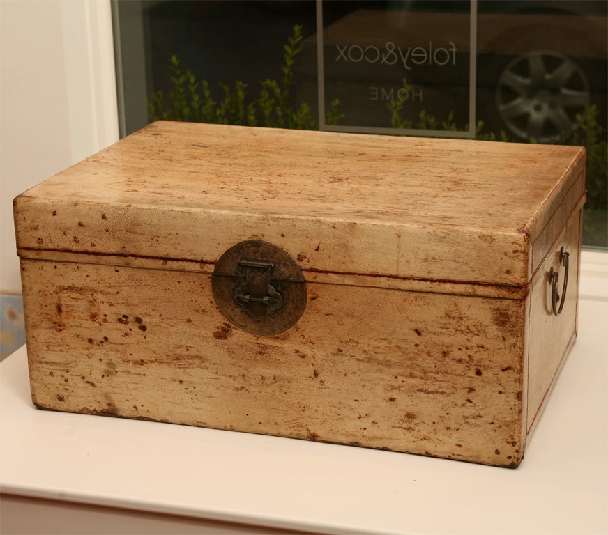 Cream vellum storage trunk with metal handles and metal pin lock featuring a round escutcheon with a delicately etched pattern.  Lined with blue cotton fabric.