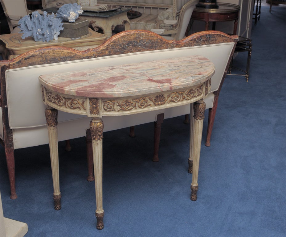 The demilune marble top above a shell and acanthus scrolled frieze raised on tapering fluted legs with foliage capitals terminating on acanthus carved feet. Stamped JANSEN.