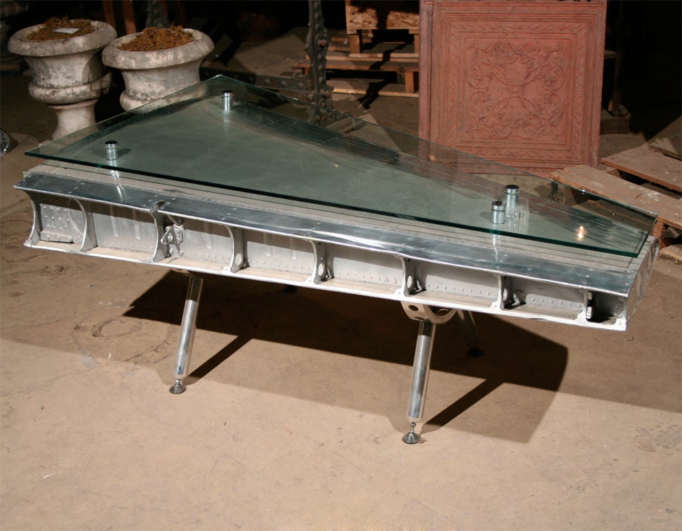 Unusual coffee table fashioned from the high polished tail fin of an English airplane with attached custom adjustable prop legs and floating glass top.