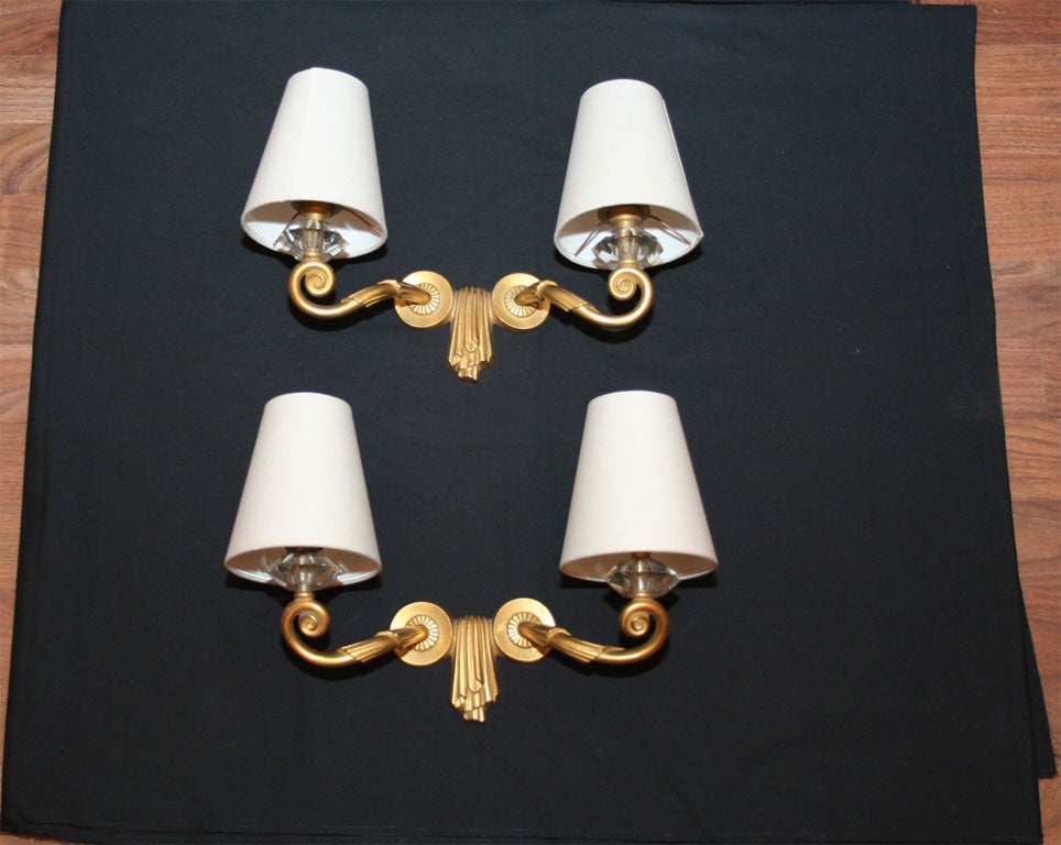 A pair of French Art Deco "Draperie" wall sconces by Jules Leleu, two-armed, in gilt bronze, crystal and fabric shades.