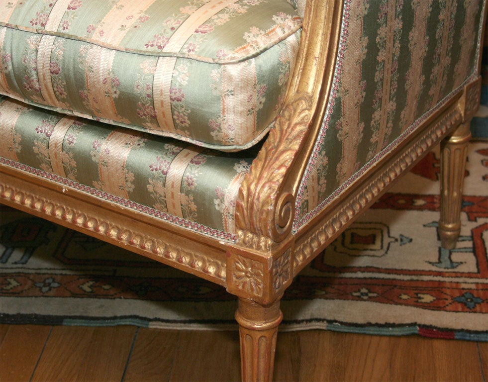A French Louis XVI style marquise with neoclassic design carved and gilt wood frame with beaded detail and scroll and acanthus leaf detail above round tapered stop fluted legs now upholstered in French silk stripe.