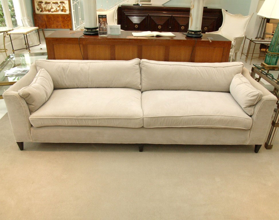 Elegant long low sofa consisting of two seat and back cushions; recently upholstered in ecru cotton velvet; square tapered legs in a walnut stain.