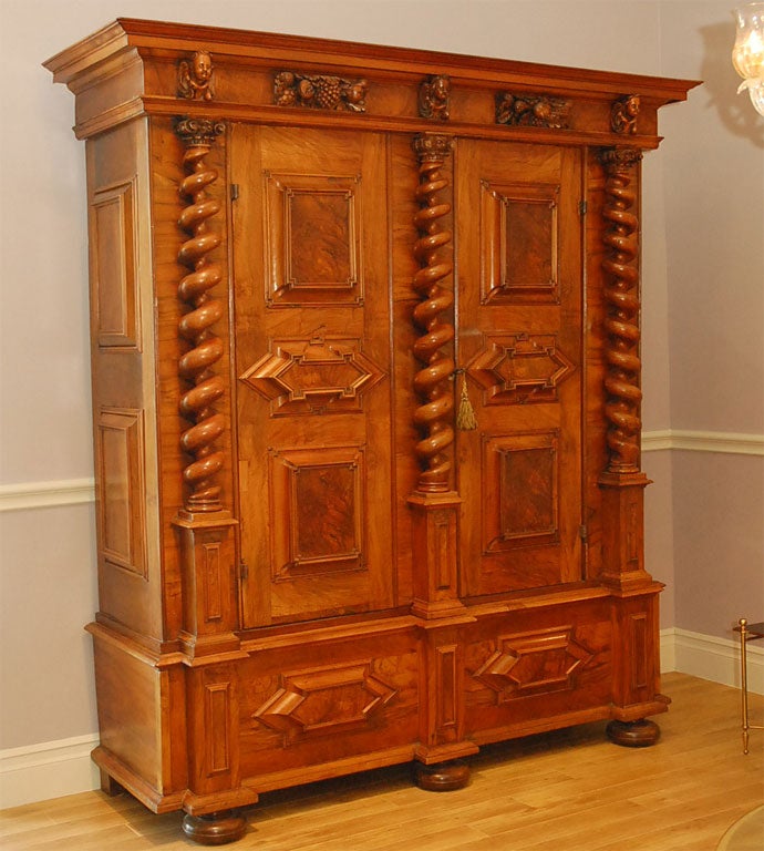 The oversailing multiple stepped and carved molded cornice above rectangular molded panel frieze over a pair of paneled doors flanked and divided by disengaged spiral twist column stiles, the lower section fitted with similar frieze above bun feet.
