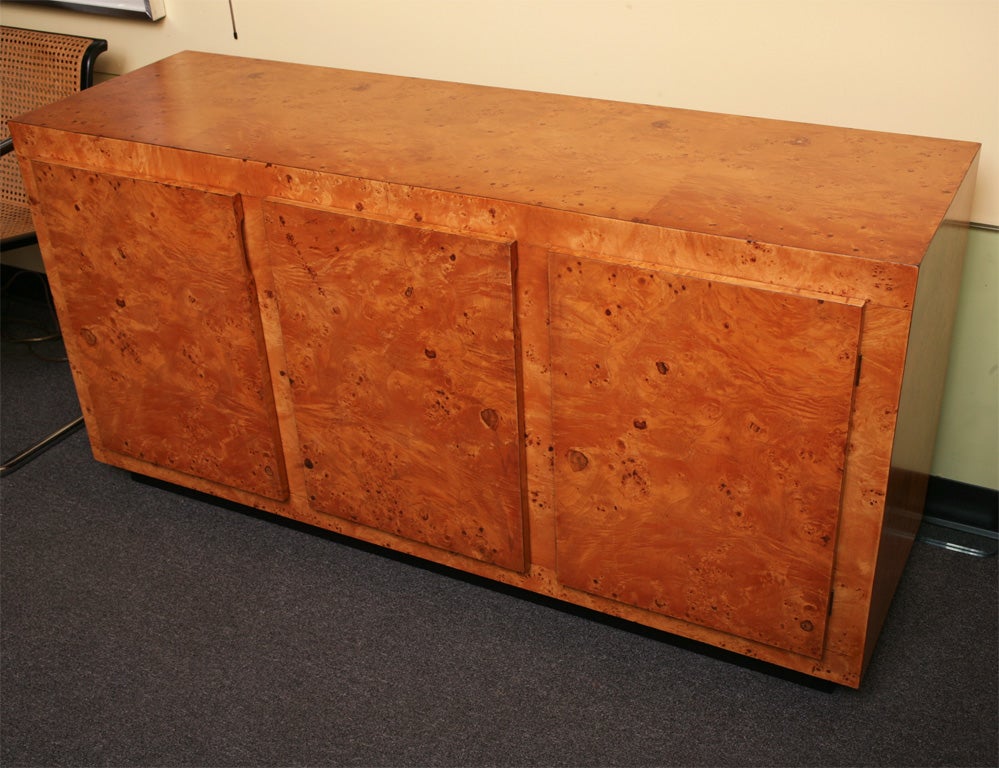 SOLD JULY 2010 Milo Baughman's signature styling and use of warm olive burl make this a commanding case piece for use a sideboard buffet or credenza.  Three doors open to reveal shelves and three black patinated shaped front deep drawers.  Resting