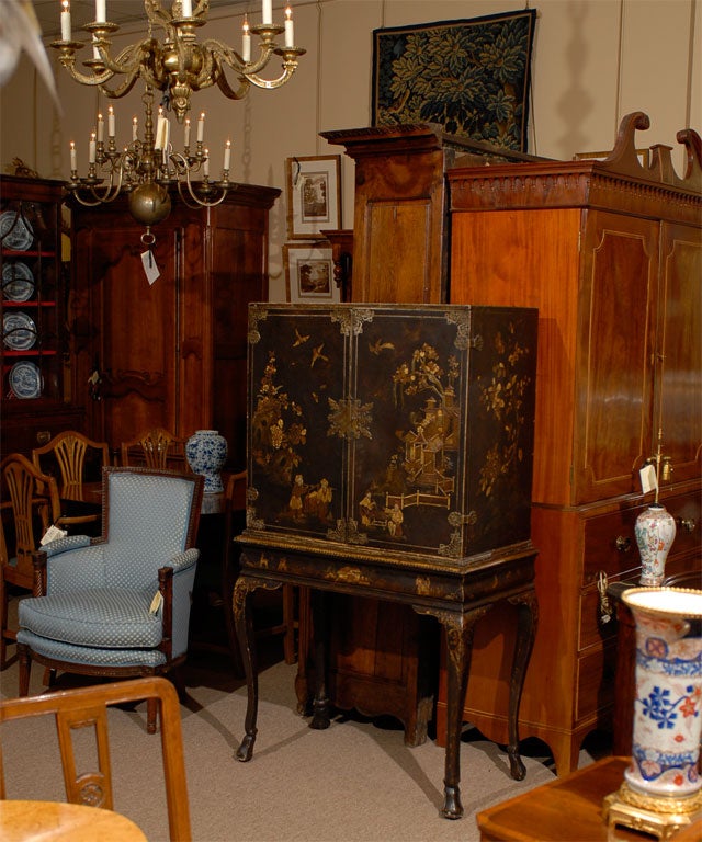 A Queen Anne style Cabinet-on-Stand, the exterior with Chinoiserie decoration on a Black Lacquer ground. Dating from the end of the 1800s, and originating in England.  <br />
<br />
The Cabinet in rectangular form, fronted by a pair of hinged