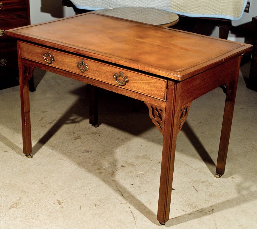 Georgian mahogany single drawer writing table with open fret corner brackets. Gold tooled saddle tan leather top; brass drawer pulls. Straight legs with corner beading end on semi-concealed brass casters.
