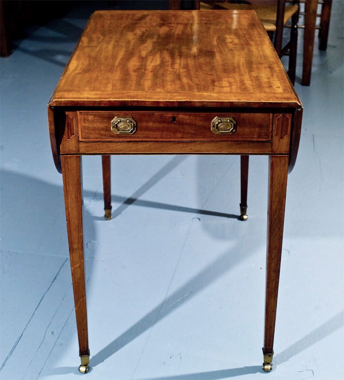 English mahogany Pembroke table on tapered legs ending in brass toecaps and casters. Satinwood cross banded drawer with brass pulls having octagonal backplates. Ebony and boxwood stringing on front, boxwood stringing on legs. Top crossbanded in