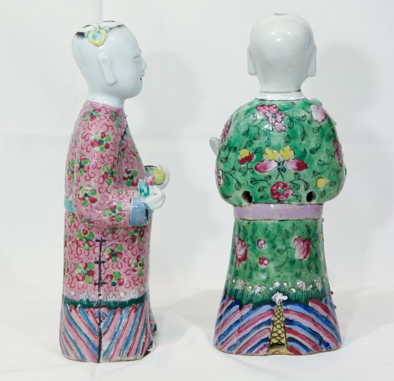 This Chinese Export, Famille Rose pair of figures of Laughing Boys in brightly colored robes, are offering traditional gifts in their outstretched arms.