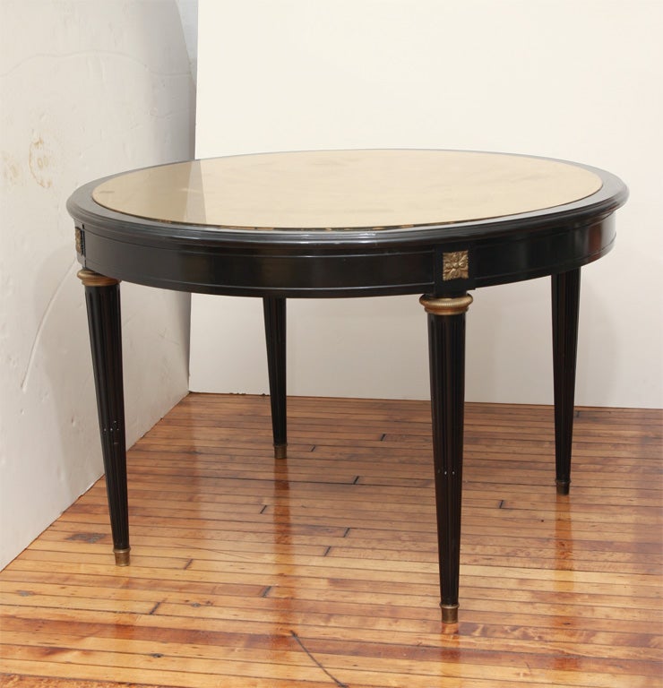 Ebonized and bronze mounted circular center table in the Louis XVI-style with gold  eglomise top. Fluted legs mounted with bronze capitals and apron inset with gold decoration.