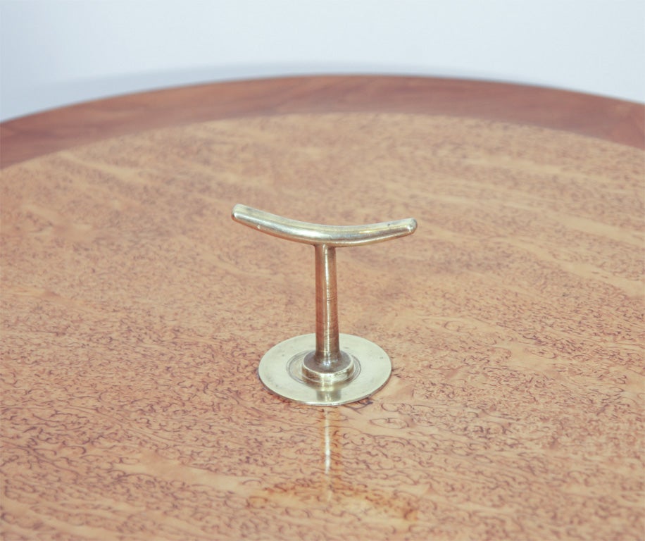 The circular top, with slightly raised lip in a burled veneer, with a brass handle in the centre, raised on a tapering stem and brass tripod foot.