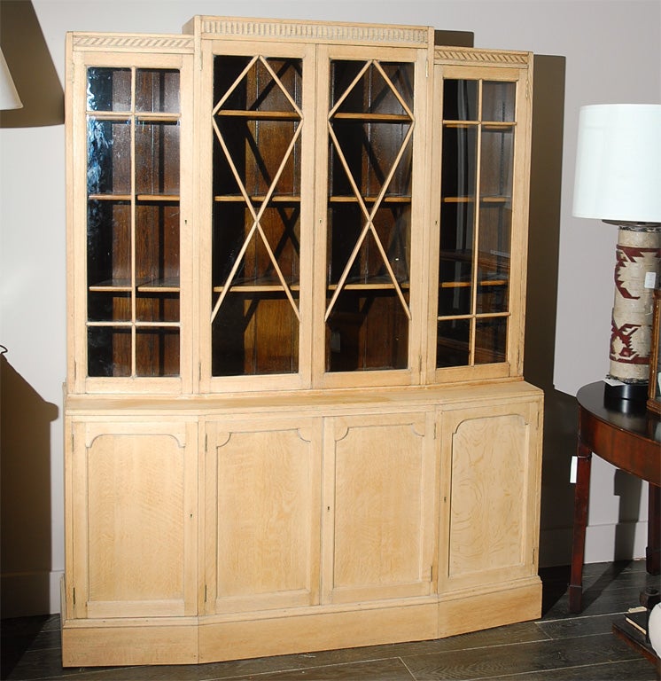 1930s art deco large oak bookcase by distinguished English furniture maker Heals. Handsome breakfront top is carved with a dentil molding frieze over glass upper doors above four carved paneled doors on a plinth base. A great piece for displays. Can