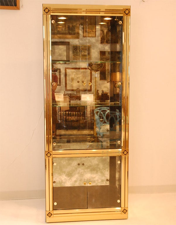 Pair of Empire-style brass vitrines with antique mirrored backs by Mastercraft.  The interior has glass shelves and the vitrines are illuminated.