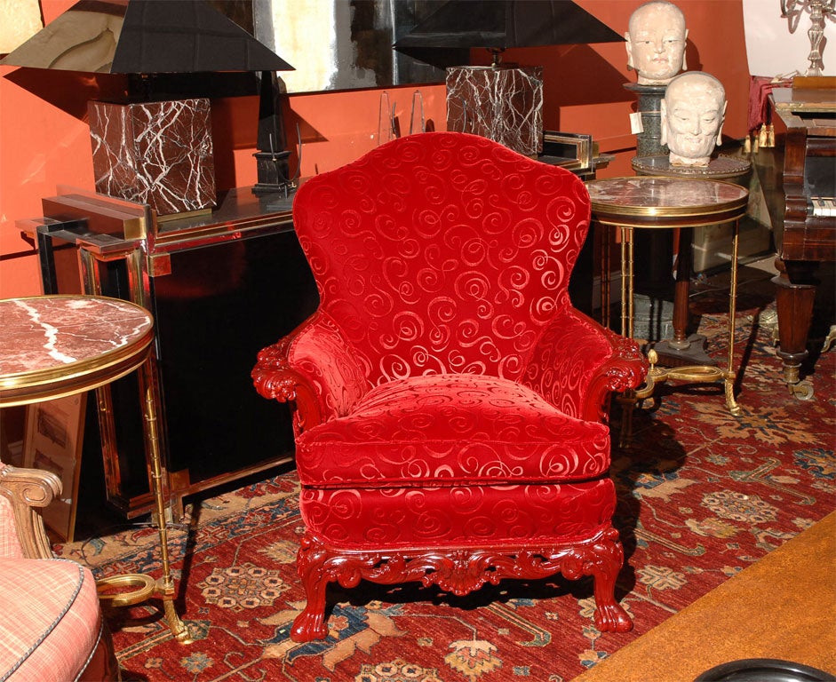 With vibrant red velvet upholstery, the shaped top above a curved back terminating at a cushioned seat; and the arms and legs carved and lacquered red.
