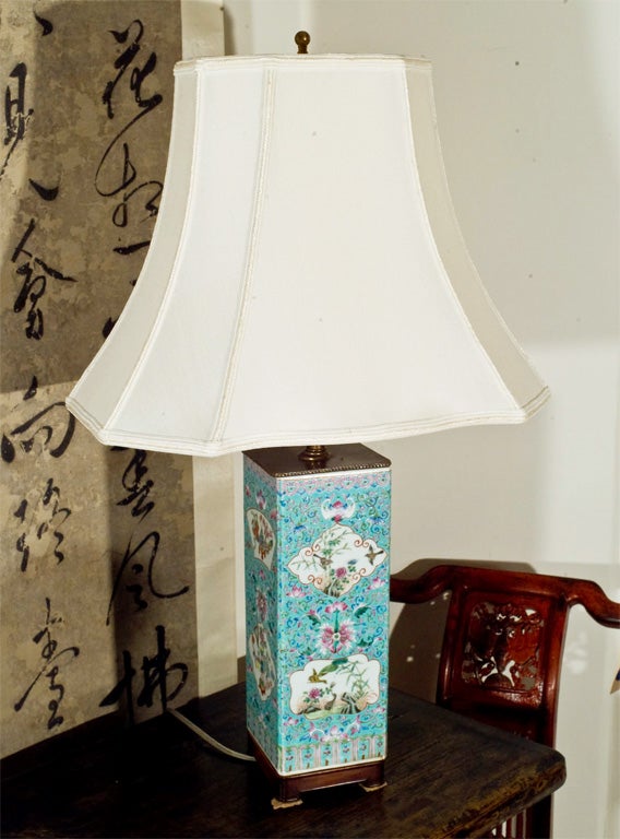 A table lamp, converted in the 30's from a 19th Century porcelain vessel, delicately painted in famille rose over a turquoise background and seated on a custom rosewood stand. New Shade.