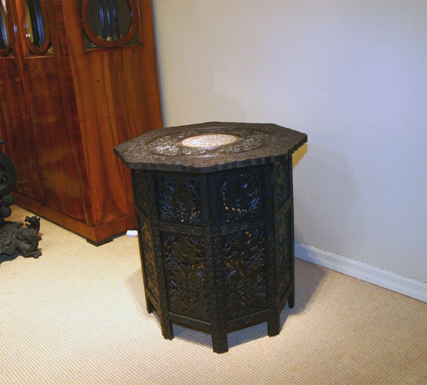 One of a near pair of carved octagonal tables, the top consisting of tripartite design of floral, leaf and inlaid bone resting on pierced foliate folding base.  The other table is the same size, color, shape with the same carving on the base,