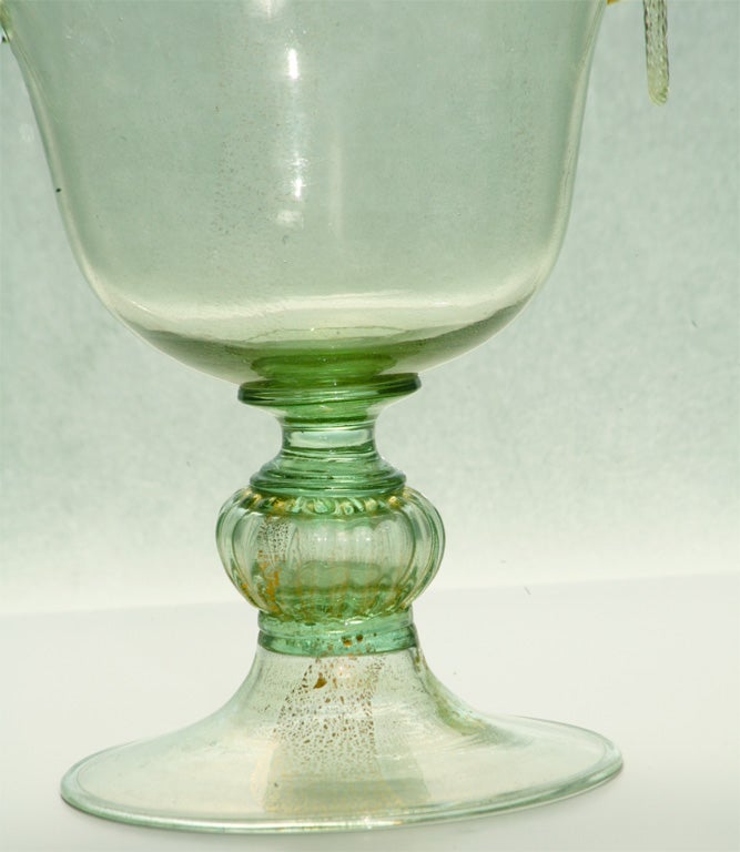 Lovely handblown green footed centerpiece with gold leaf inclusions throughout. This graceful piece can Stand alone or used as a center bowl filled with flowers or fruit. It is accented with applied glass handles and twisted 