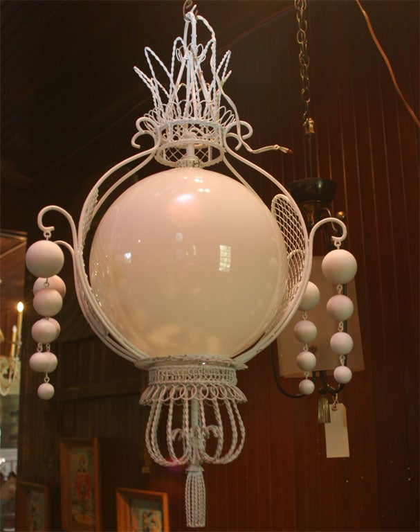 Fanciful wire chandelier with central glass globe and white painted wood ball tassels.