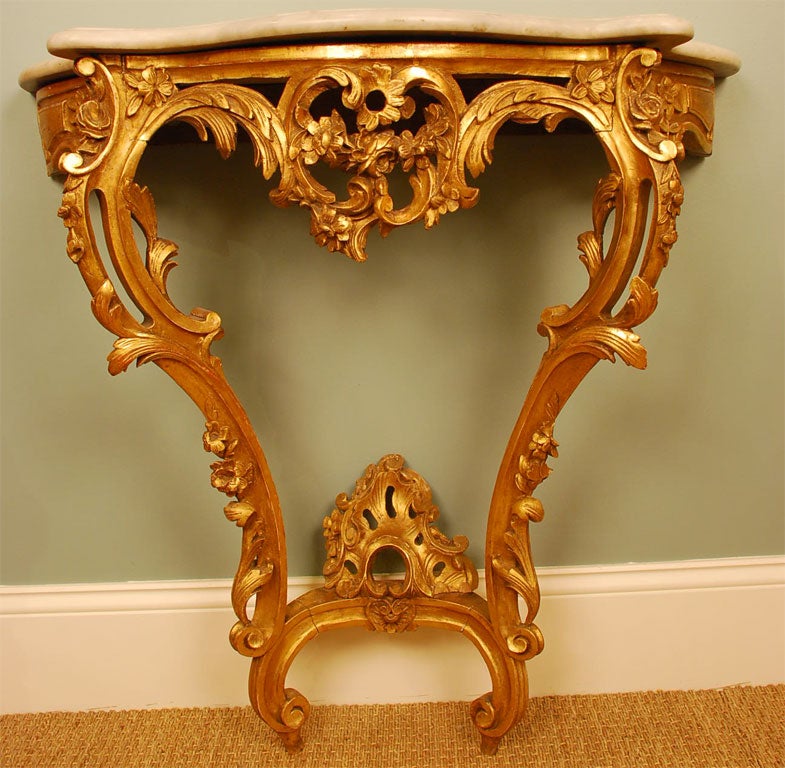 Louis XV style giltwood console table with white marble top. Elegant carved details include shell and leaf forms, flowers and other Rococo ornamentation.