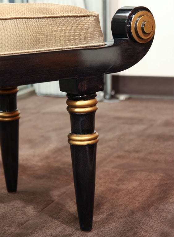 Stylized bench in ebonized walnut<br />
with antique gold leaf details.<br />
Has scroll design and tapered<br />
legs with gold leaf banding.<br />
The seat is slightly tufted <br />
with button details.