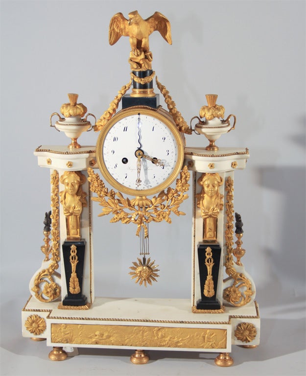 A fine Louis XVI portico mantel clock. Ormolu, white marble and enamel. Drum-shaped ormolu clock case surmounted by an ormolu eagle is flanked by two marble pillars. Above and below are swags with flowers, wine and oak leaves. Each pillar is