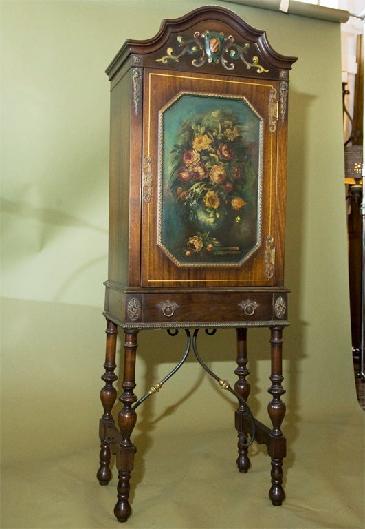 Beautiful, tall, narrow cabinet with single drawer.  It is ideal for sheet music, paper, linens, or other storage.  Decorative floral still-life, ornate hardware and polychromed details are featured. The iron and brass stretcher is a hallmark of the