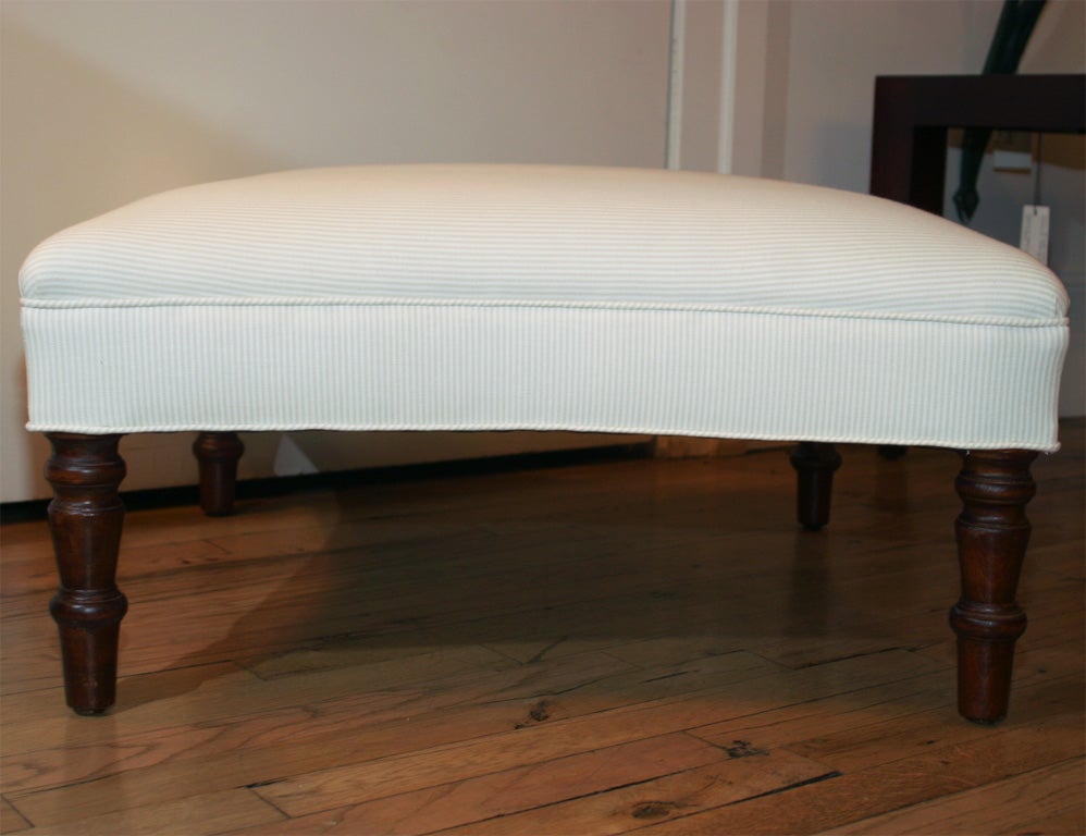 Ottoman with slightly curved sides on mahogany turned legs, upholstered in 100% cotton ticking fabric. Pair available.
