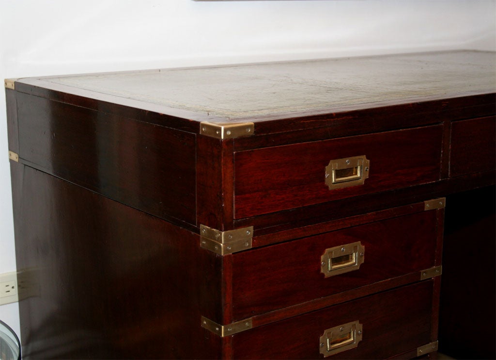 An English mahogany campaign style knee hole desk with nine drawers and brass bound corners supported by bracket feet and having inset tooled leather top and recessed brass pulls.