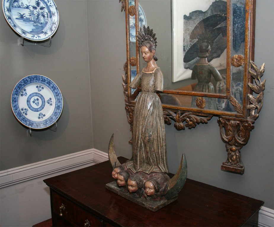 Exceptional Spanish Colonial gilt and painted wood figure of the Madonna, standing in a long gown with glass eyes and silver halo, on a crescent moon emblazoned with four cherubim, on rectangular wooden base. This piece is an unusual blend of