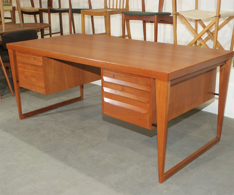 Sleek and stunning teak desk by Kai Kristiansen. Features a floating design, 3 drawers with full width tab pulls, a filing cabinet, brass keyholes, and 2 additional lockable cabinets in the front for extra storage.  Generously proportioned.