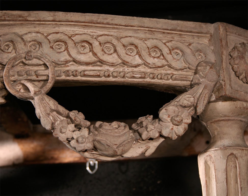 A very fine painted and carved wood Louis XVI demilune console with marble top above guilloche frieze with hanging garlands supported by Tapered Fluted Feet Joined by Fluted Stretcher Centered by Classical Urn Trophy.