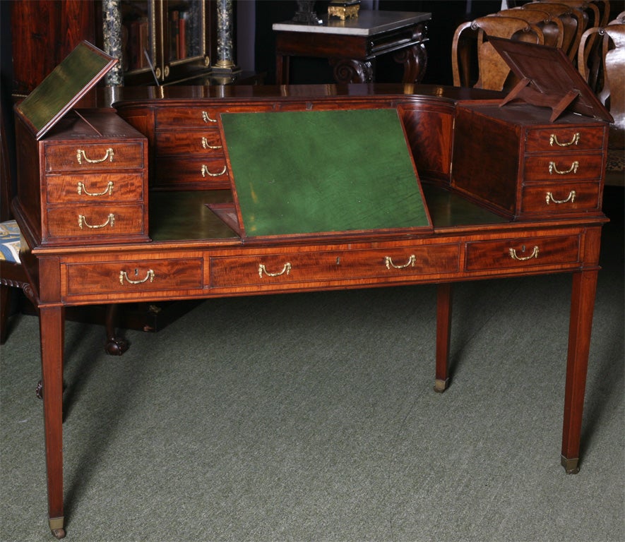 An English 19th century Carlton House desk. The desk is in mahogany with woderful flame mahogany panels to the back. The desk has sloped writing surfaces in the center and also on the wings of the desk, these were possibly for clerks to take notes
