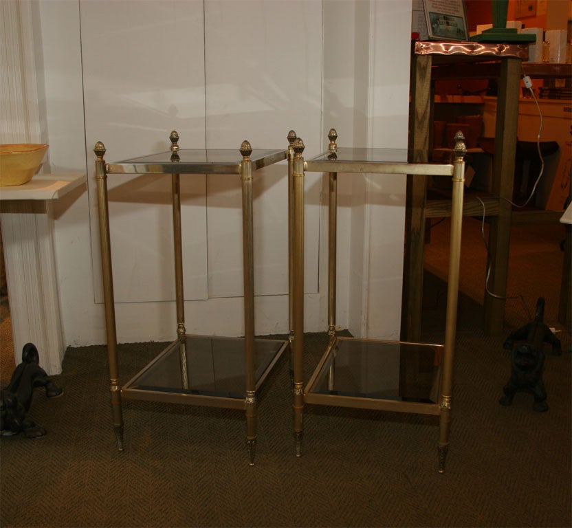 Lovely pair of brass end tables with two levels of beveled smoked glass, legs are topped with pineapple finials, symbolic of welcome & hospitality