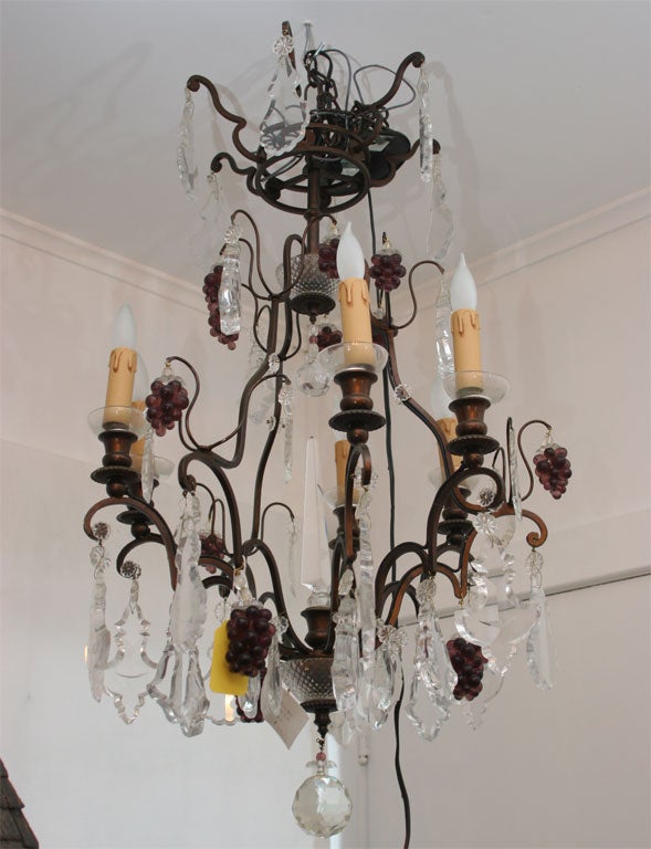 Elegant iron chandelier with crystal drops and bunches of glass grapes.