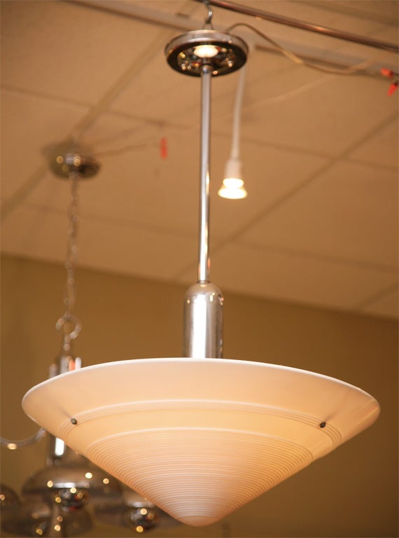 Sleek period streamline moderne light featuring a wide conical thick milk glass bowl with concentric ribs in the glass suspended under a chromed bullet shaped socket housing, chrome pole and ceiling cap. Machine Age clean, minimal lines with a