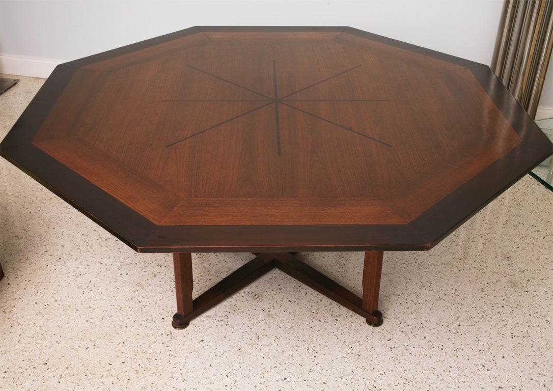 The octagonal top with a dark walnut band and line inlay on a mahogany field over tapering legs joined by a cross stretcher with leather accents, the whole on round brass elements- this table was manufactured as a small low table and was custom made