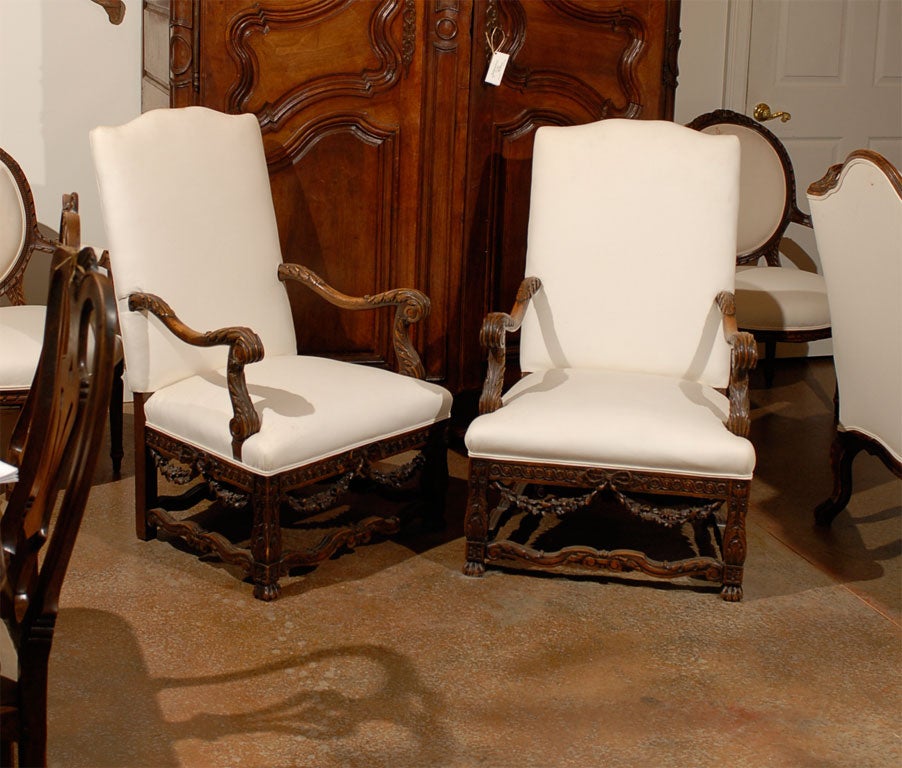 An unusual pair of French walnut Louis XIV style armchairs from the mid-19th century, with tall backs, scrolled arms, new upholstery and richly carved base showing a Louis XVI influence. Each of this pair of French fauteuils features a tall slanted
