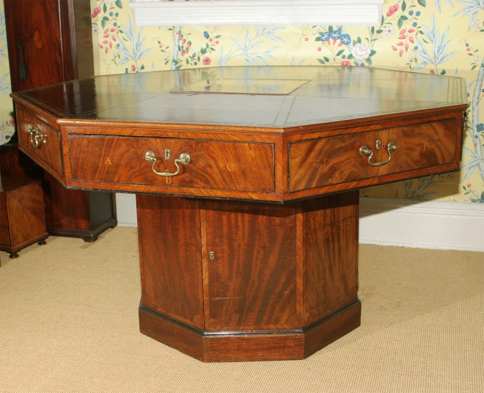 A rare George III mahogany rent table. The revolving, gilt tooled leather inset octagonal top having a secret central hinged compartment of finely figured mahogany that opens to reveal a locked mahogany lined money well. The frieze containing eight