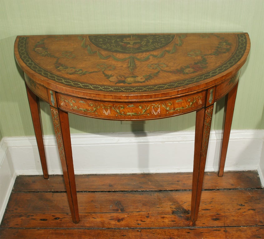 Beautifully painted Sheraton period satinwood demilune card table, the top having a still life of fruits in a basket above a garland of roses centered with cornucopia, foliate scrolls and swags below bordered by garlands of flowers joined by