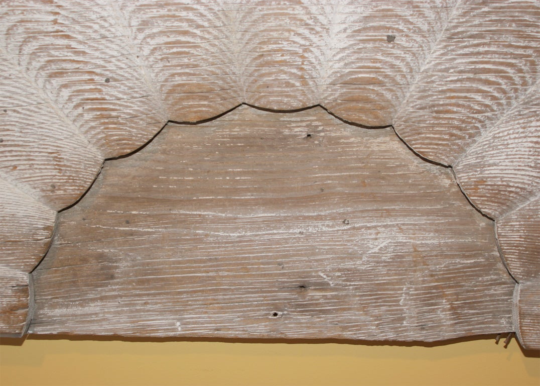 Scalloped half-round fan light with weathered surface, old white paint and exposed natural wood grain.