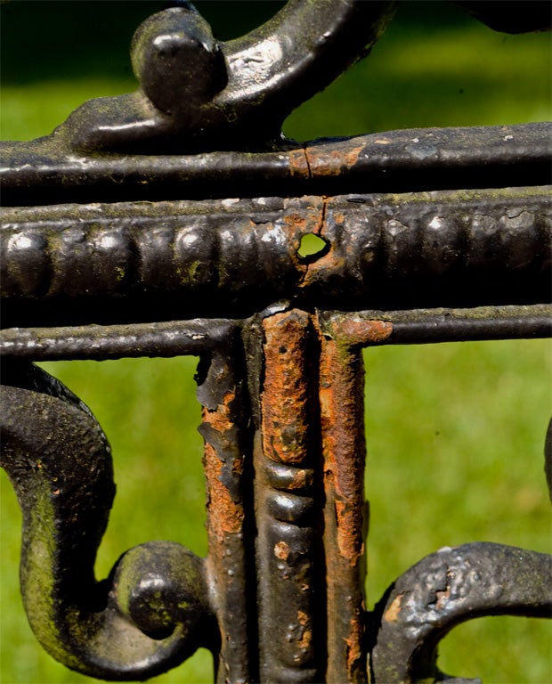 A cast-iron seat in the curtain style, the back with foliate scrolls and rosette medallions, the seat and apron pierced.