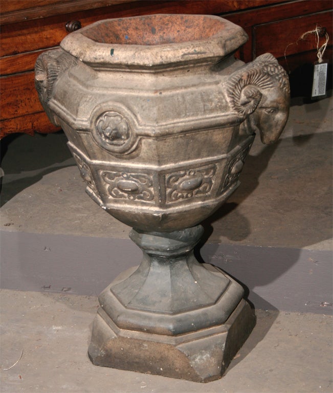 English Arts and Crafts stoneware urn of hexangular shape with ram’s heads handles, on conforming base.
