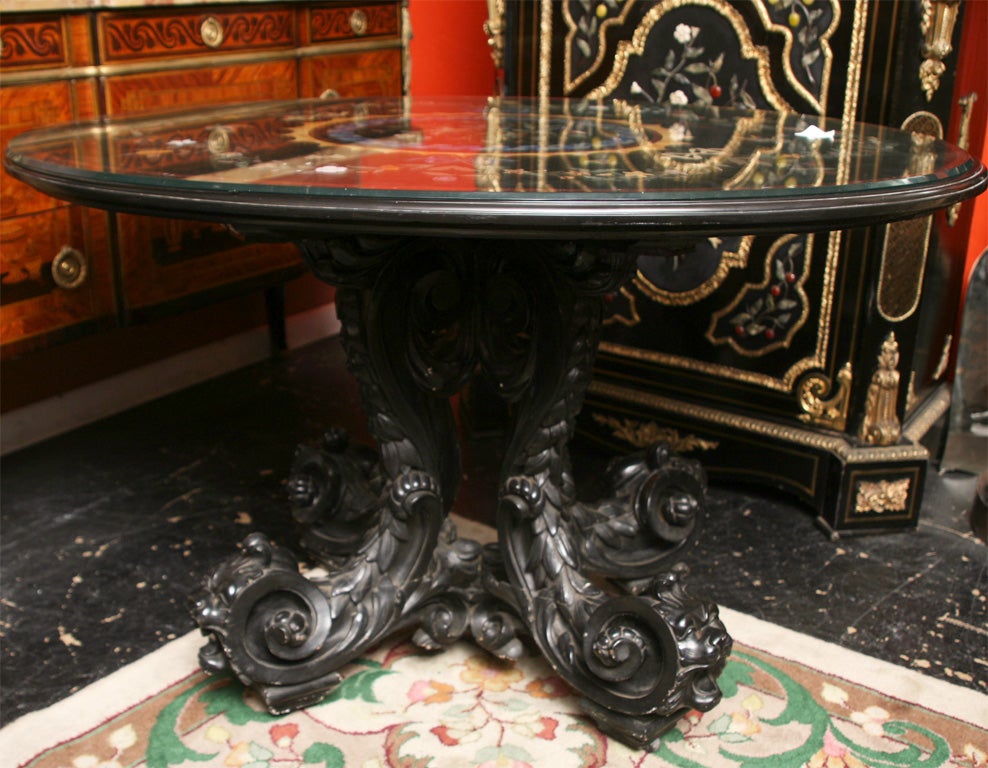A large Italian pietre dure center table, having an oval top centering a decoration with birds and flowers; the surround of garlands, ribbons, butterflies and fruit on a heavily carved ebonized wood base terminated by carved lions heads with rams